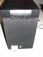 Front view of the Yamaha subwoofer showing control panel with standby, bass, high cut, and volume knobs and a large speaker covered by black mesh.