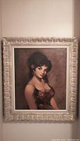 Full view of the framed portrait painting showing the ornate silver frame and the woman against a brown background.