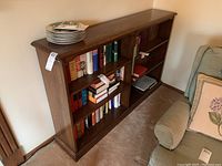 Front view showing six shelves with books and plates on top, highlighting size and condition of wood bookcase.