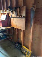 Workshop corner showing wall-mounted hand tools including hammers, handsaw, and other tools, with workbench and shelving visible.
