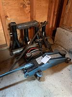Mini hydraulic floor jack and multiple metal car jack stands stored in a wooden shed corner