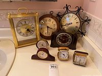 Photo of eight clocks including large gold-tone carriage clock, wooden and metal wall clocks, and four travel clocks in cases.