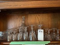 Shelf showing multiple crystal wine glasses, champagne flutes, and a decanter with a faceted stopper all arranged together.