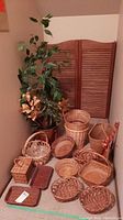 Full view of faux plant and all wicker baskets and broom on floor against wall near wooden panels.