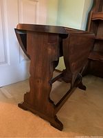Side view of the wooden table showing the decorative scalloped side supports and crossbar base.