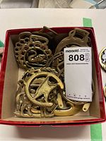 Photo showing a collection of various horse brasses in a red box.