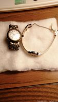 Two vintage ladies watches placed on white fabric; one with floral design band, other with slim band.