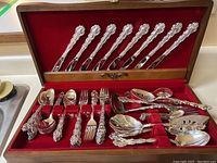 Full view of the cutlery set in the open wooden box with red velvet lining, showing multiple types of utensils organized in slots.