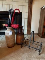 Photo showing the umbrellas placed inside two ceramic standing vases, and the metal wood holder positioned beside them on the carpet floor.