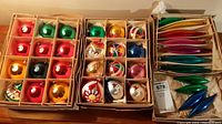 Photo showing three open boxes with divided cardboard compartments filled with assorted colorful Christmas ornaments including balls, novelty shapes, and long teardrop shapes.