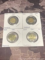 Four Canadian two-dollar coins in protective holders placed on map background, dated 1999, 2011, 2020, 2022.