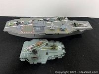 Two gray plastic aircraft carriers with multiple toy jets and one helicopter arranged on top, showing assortment and playset scale