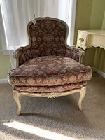 Front view of the upholstered armchair showing the patterned fabric in taupe with blue and gold and the carved light-colored wooden frame.