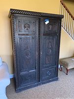 Front view of ornate carved wooden armoire showing decorative panels and two doors.