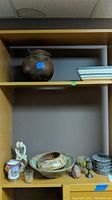 Shelf with multiple pottery items, votive holders, soapstone figurines, silver chalice