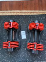 Top-down view of both Elevens adjustable hand weights showing red plates and black handles, with adjustable weight increments visible.