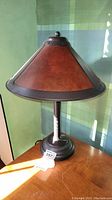 Full front view of desk lamp showing leather cone-shaped shade with metal trim and base.