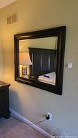 Full view of the mirror hanging on the wall showing wood frame and reflection of room elements.