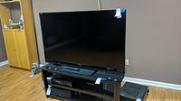 Sharp Aquos 60-inch TV on a stand with remote control on top, showing overall condition and setup.