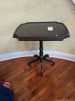Black painted pedestal side table with rounded square top showing slight wear and a marked stain on surface.