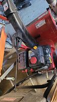 Photo showing the black chute, red engine housing, and parts of the snowblower gas engine with fuel and oil caps.