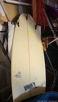 Top view of cream-colored surfboard deck showing twin fin boxes, central stringer and Al Merrick logo at tail.