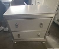 Front view of closed silver nightstand showing two drawers with chrome drop handles and the nightstand's overall shape and finish.