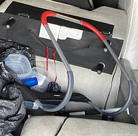 Photo showing the metal frame of the Ab Crunch with red parts and black padding in a car seat and plastic containers in the background.