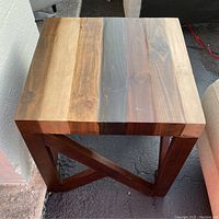 Front and top view of squared wooden end table showing thick wood plank top with natural wood finish and intersecting geometric base supports.