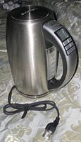 Side view of stainless steel electric kettle with attached power cord on surface