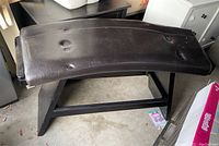 Top-down angled view of curved dark brown ultrahyde bench seat and sturdy wooden base in dark tones.