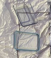 Clear rectangular glass container with matching clear lid featuring a blue seal, laid out on a light background.