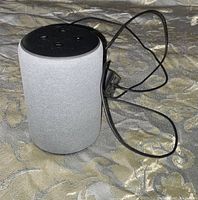 Heather gray Amazon Echo 3rd gen smart speaker upright on patterned fabric surface with power cord attached