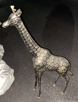 Photo of a dark silver giraffe statue with gold scale patterns showing the side profile and details of the giraffe's body and neck.