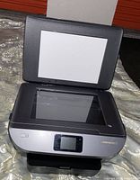 Photo showing the HP Envy 7155 printer with scanner lid open, front touchscreen display visible.