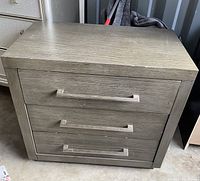 Front view of gray wooden nightstand showing three large drawers and rectangular handles.