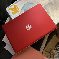Red HP laptop closed showing top cover with HP silver logo.