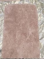 Rectangular rose colored bathroom rug with soft shag texture, shown on shiny surface.