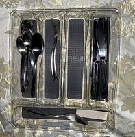 Silverware organized in a clear plastic tray with multiple compartments, containing small spoons, forks, two types of knives, and black chopsticks, all silver-toned with a polished finish.