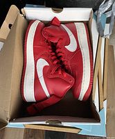 Pair of red and white Nike Air Force 1 High Retro QS sneakers inside original box, viewed from above.