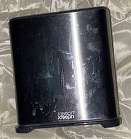 Front and side view of Joseph Joseph stainless steel kitchen utensil holder showing silver finish with smudges and imprint logo