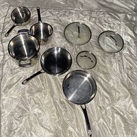 Full set of stainless steel pots and pans arranged with glass lids to show quantity and condition