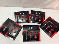 Five Dior Rouge Ultra Rouge lipstick sample packets arranged on a white surface with red and black packaging displaying lip color swatches and lip brush illustrations.