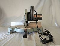 Full side view of the Delta miter saw showing power cord and handle, metal base and saw blade area.