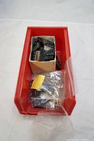 Red bin containing cardboard box with multiple black digital chip plates and loose parts in plastic bags inside bin.