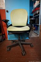 Front view of the office chair showing light green fabric upholstery on the seat and backrest, black armrests, and caster wheels.