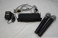 Front view of Samson UR1 True Diversity wireless microphone receiver with two handheld microphones and cables.