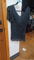 Front view of black beaded and sequined Adrianna Papell Boutique top on hanger showing V-neck and slit shoulders