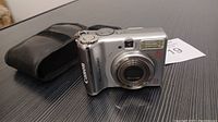 Canon PowerShot A560 camera front view with soft black carrying case visible in background on table surface.