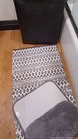 Black woven clothes hamper with black and white geometric patterned rug on wooden floor.